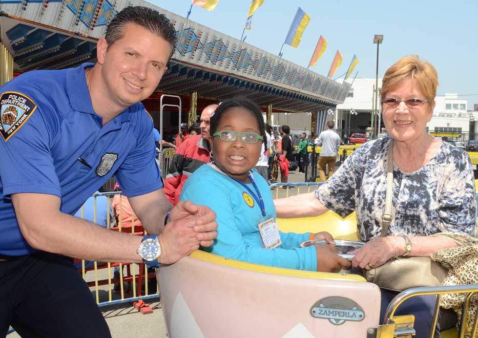 NYPD Volunteer with child and chaperone enjoying a ride at an amusement park